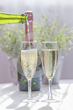 Wedding concept and celebration. Serving yellow and bubbly champagne in two glass cups, a green bottle in the background