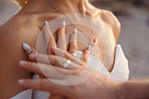 Wedding concept, couple touching their hands with wedding ring bands. Sea necklace. Loving married young couple.