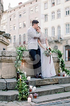 Wedding concept. The happy romantic wedding couple are standing on the stone stairs in front of old city buildings