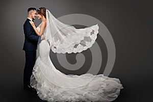 Wedding Couple, Beautiful Bride in White Dress and Long Veil, Elegant Groom Kissing Romantic Studio Portrait