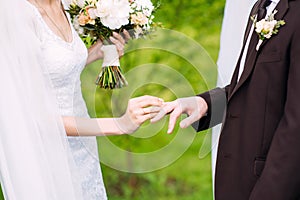 Wedding couple. Bride and fiance at outdoor wedding ceremony. Bride putting golden ring on groom`s finger on green grass backgroun