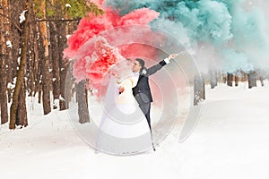 Wedding couple with color smoke in the winter park. Colour bomb