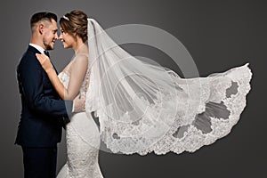 Wedding Couple Dancing. Romantic Bride and Groom Portrait. Bridal long Veil flying over Gray Studio Background