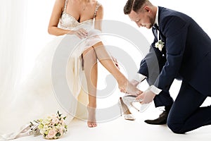 Wedding Couple, Elegant Groom in Suit wearing shoe to Bride Leg in White Dress