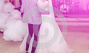 Wedding couple first dance. Bride and groom are hugging. White decorative smoke. Happy emotions. Beautiful long sleeve dress