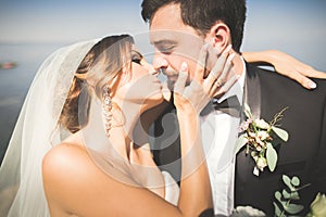 Wedding couple, groom, bride with bouquet posing near sea and blue sky