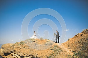 Wedding couple, groom, bride with bouquet posing near sea and blue sky