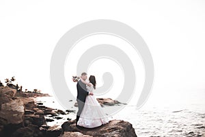 Wedding couple, groom, bride with bouquet posing near sea and blue sky