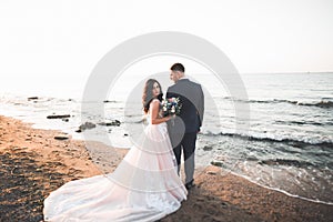 Wedding couple, groom, bride with bouquet posing near sea and blue sky