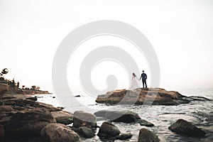 Wedding couple, groom, bride with bouquet posing near sea and blue sky