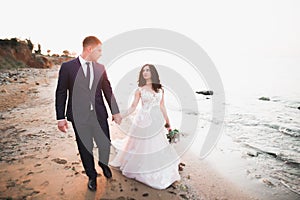 Wedding couple, groom, bride with bouquet posing near sea and blue sky