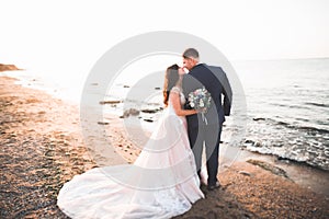 Wedding couple, groom, bride with bouquet posing near sea and blue sky