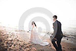 Wedding couple, groom, bride with bouquet posing near sea and blue sky