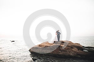 Wedding couple, groom, bride with bouquet posing near sea and blue sky