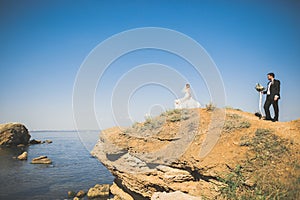 Wedding couple, groom, bride with bouquet posing near sea and blue sky