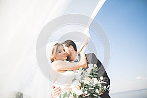 Wedding couple, groom, bride with bouquet posing near sea and blue sky