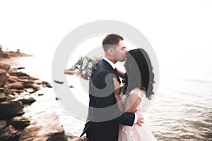 Wedding couple, groom, bride with bouquet posing near sea and blue sky