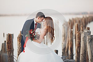 Wedding couple, groom, bride with bouquet posing near sea on sunset