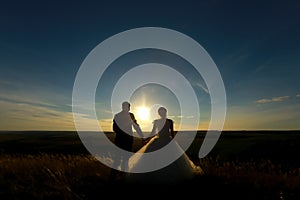 Wedding couple hold hands on the sunset. Silhouette of Bride and Groom