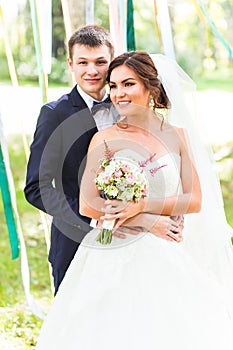 Wedding couple hugging, bride holding a bouquet of flowers, the groom embracing her