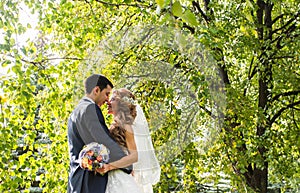 Wedding couple hugging, the bride holding a bouquet of flowers, groom embracing her