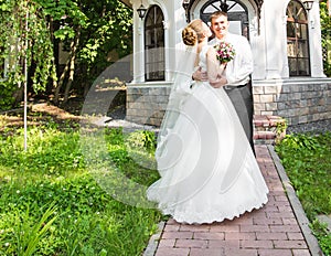 Wedding couple hugging, the bride holding a bouquet of flowers, groom embracing her outdoors