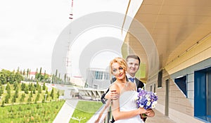 Wedding couple hugging, the bride holding a bouquet of flowers, groom embracing her outdoors