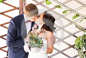 Wedding couple kissing, bride holding fan of peacock feathers, the groom embracing her