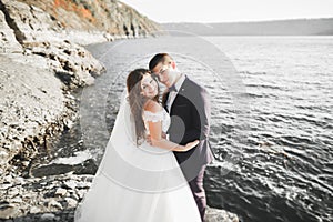 Wedding couple kissing and hugging on rocks near blue sea