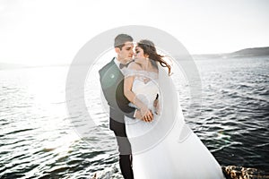 Wedding couple kissing and hugging on rocks near blue sea