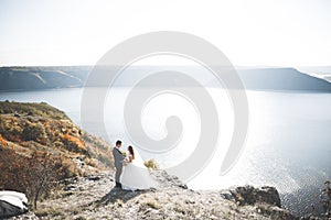 Wedding couple kissing and hugging on rocks near blue sea