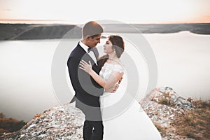 Wedding couple kissing and hugging on rocks near blue sea