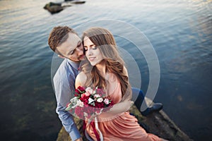 Wedding couple kissing and hugging on rocks near blue sea