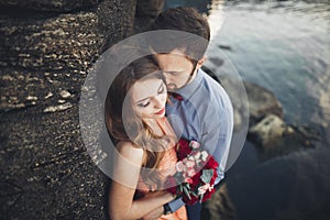 Wedding couple kissing and hugging on rocks near blue sea