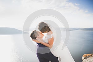 Wedding couple kissing and hugging on rocks near blue sea