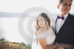 Wedding couple kissing and hugging on rocks near blue sea