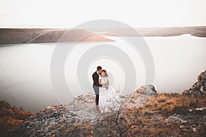 Wedding couple kissing and hugging on rocks near blue sea