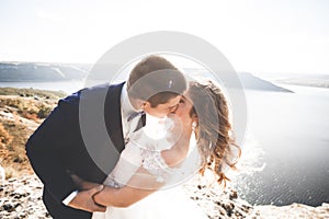 Wedding couple kissing and hugging on rocks near blue sea