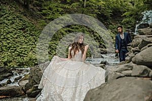 Wedding couple near a mountain river. She is in the foreground in focus. Groom and bride. Wedding photo session in nature. Photo