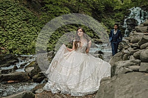 Wedding couple near a mountain river. She is in the foreground in focus. Groom and bride. Wedding photo session in nature. Photo