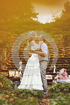 Wedding couple in a rustic style kissing near the stone steps surrounded by wedding decor at autumn forest