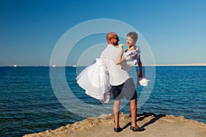 Wedding couple at sea shore, blue water and sky background, beautiful wife in white dress and handsome young husband in stylish