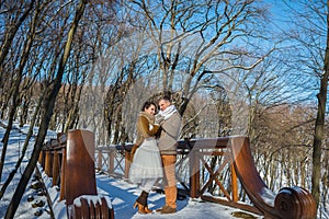 Wedding couple in a showy wither day, holding each other, standing on the bridge. rustic style. short wedding dress. Girl brunette