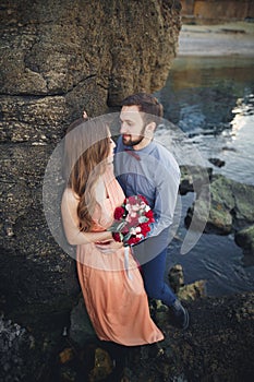 Wedding couple sitting on large stone around blue sea