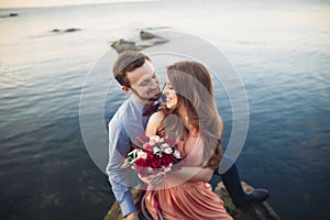 Wedding couple sitting on large stone around blue sea