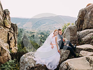 Wedding couple sitting at rocky mountains against the sky. Cute romantic moment.