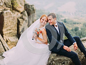 Wedding couple sitting at rocky mountains against the sky. Cute romantic moment.