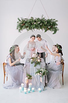 Wedding couple smiling at the decorated wedding table. Bridesmaids and groommen drink champagne sitting at the table in