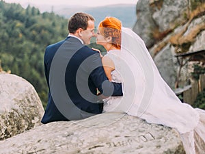 Wedding couple softly embracing at rocky mountains against the sky. Cute romantic moment.