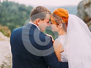 Wedding couple softly embracing at rocky mountains against the sky. Cute romantic moment. Back view